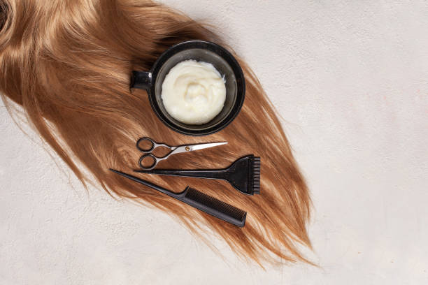 Blonde hair with scissors, comb, tint brush, and dye bowl for hair dyes.